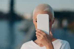 Short haired woman covering her face with smartphone. Mobile phone data security, privacy and