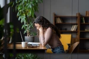 Young frustrated female employee in front of laptop at workplace, getting stuck on task or project