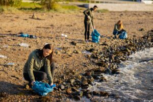 Social Responsibility: Dedicated woman in a team picking up garbage in bag at beach