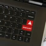 Laptop on workspace area with cyber security red keyboard key with Spam Alert warning written on it